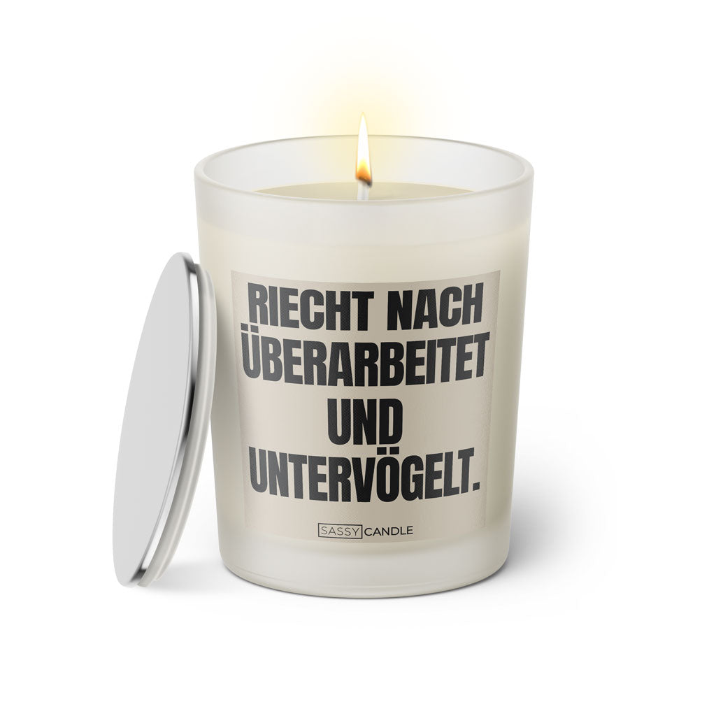 Duftkerze mit witzigem Spruch: Riecht nach untervögelt und überarbeitet. Farbe beige und schwarze Schrift. Kerzenglas mit silbernem Deckel von SassyCandle.