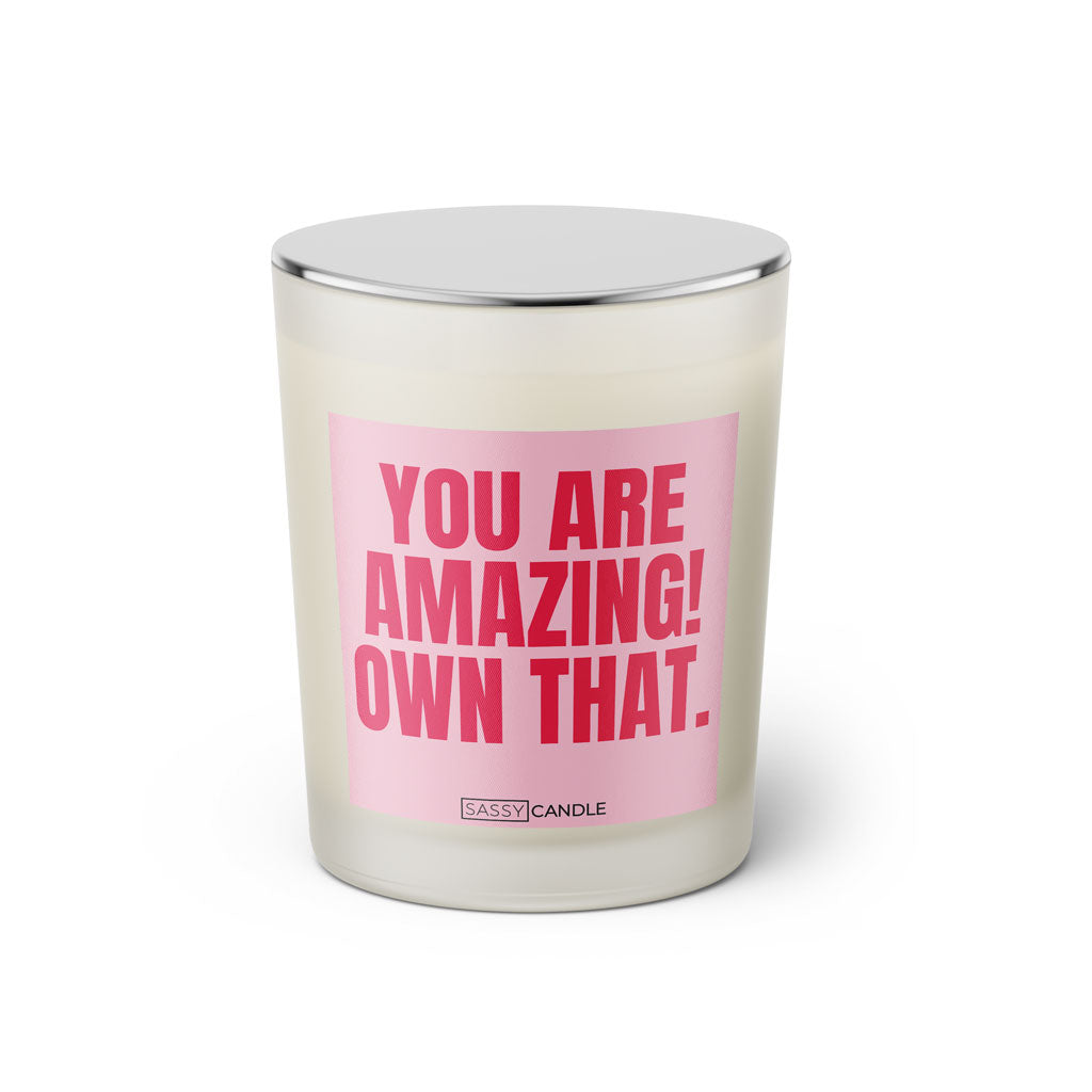Duftkerze mit witzigem Spruch: You are amazing! Own that. Farbe rosa und pinke Schrift. Kerzenglas mit silbernem geschlossenem Deckel von SassyCandle.