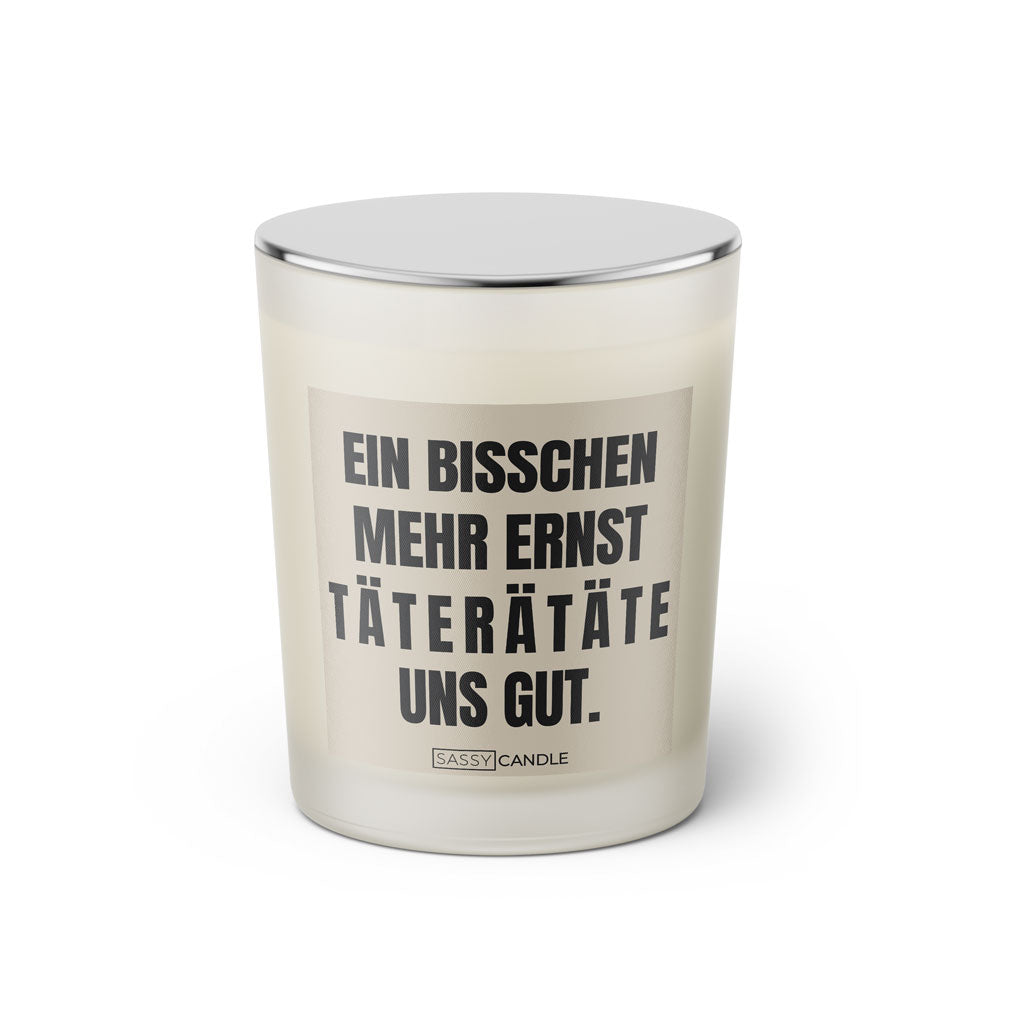 Duftkerze mit witzigen Spruch: Ein bisschen mehr Ernst taterätäte uns gut. Kerzenglas mit silbernen Deckel von Sassy Candle. Farbe beige und schwarz.