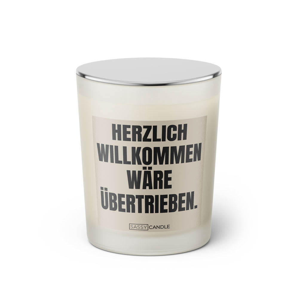 Duftkerze mit witzigem Spruch: Herzlich Willkommen wäre übertrieben. Farbe beige und schwarze Schrift. Kerzenglas mit silbernem geschlossenem Deckel von SassyCandle.