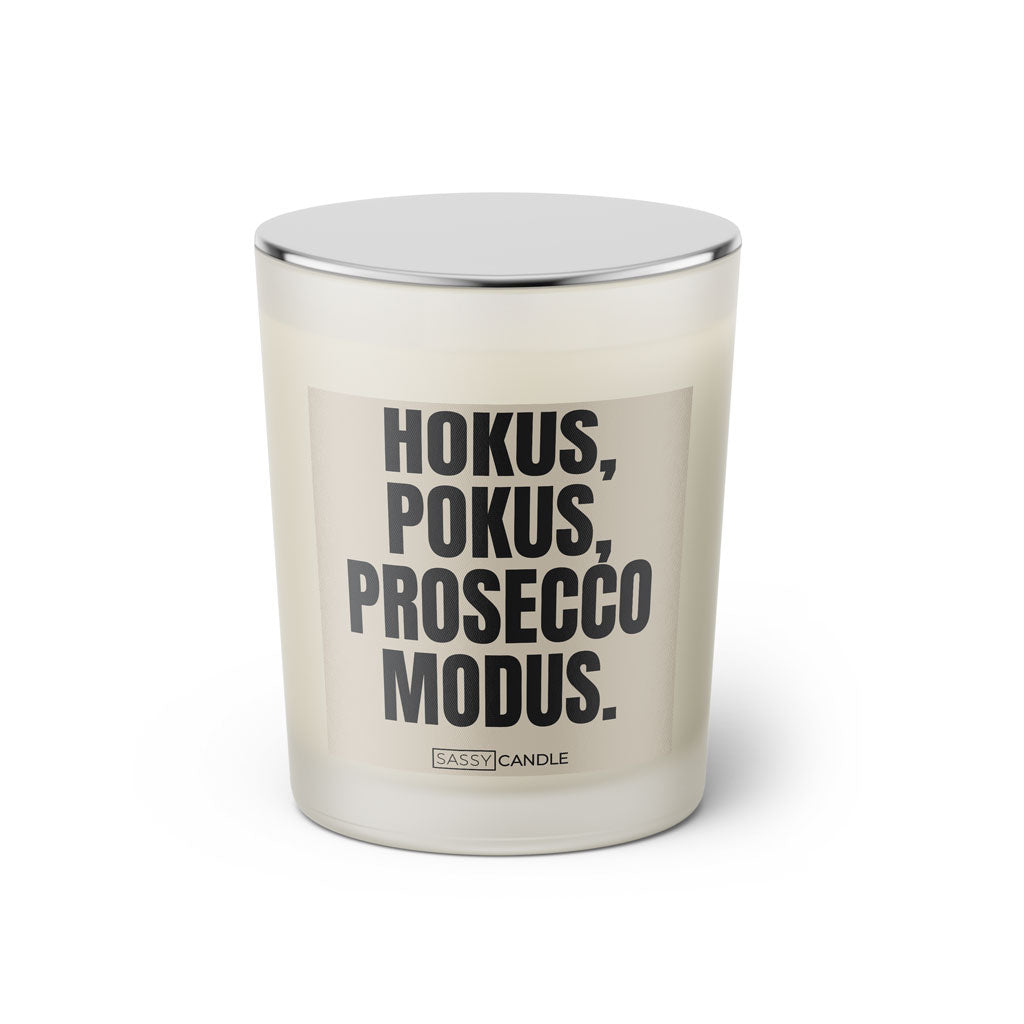 Duftkerze mit witzigem Spruch: Hokus Pokus Prosecco Modus. Farbe beige und schwarze Schrift. Kerzenglas mit silbernem geschlossenem Deckel von SassyCandle.