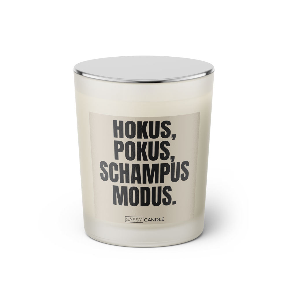 Duftkerze mit witzigem Spruch: Hokus Pokus Schampus Modus. Farbe beige und schwarze Schrift. Kerzenglas mit silbernem geschlossenem Deckel von SassyCandle.