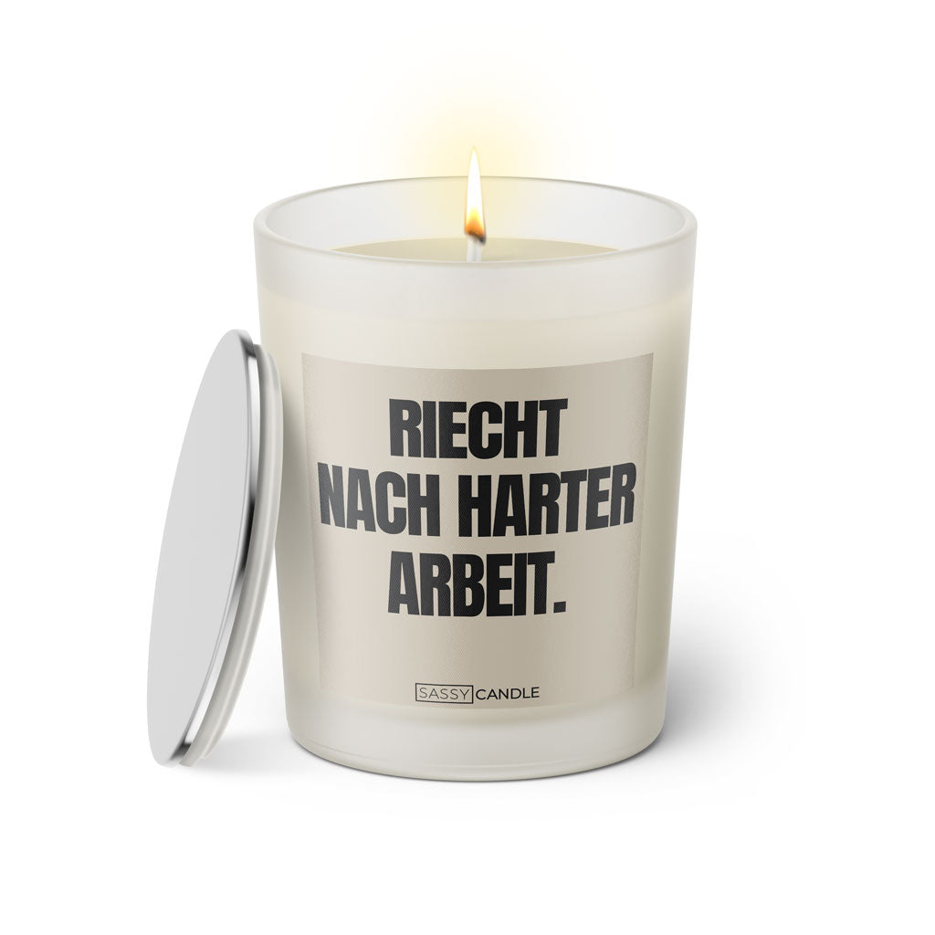 Duftkerze mit witzigem Spruch: Riecht nach harter Arbeit. Farbe beige und schwarze Schrift. Kerzenglas mit silbernem Deckel von SassyCandle.