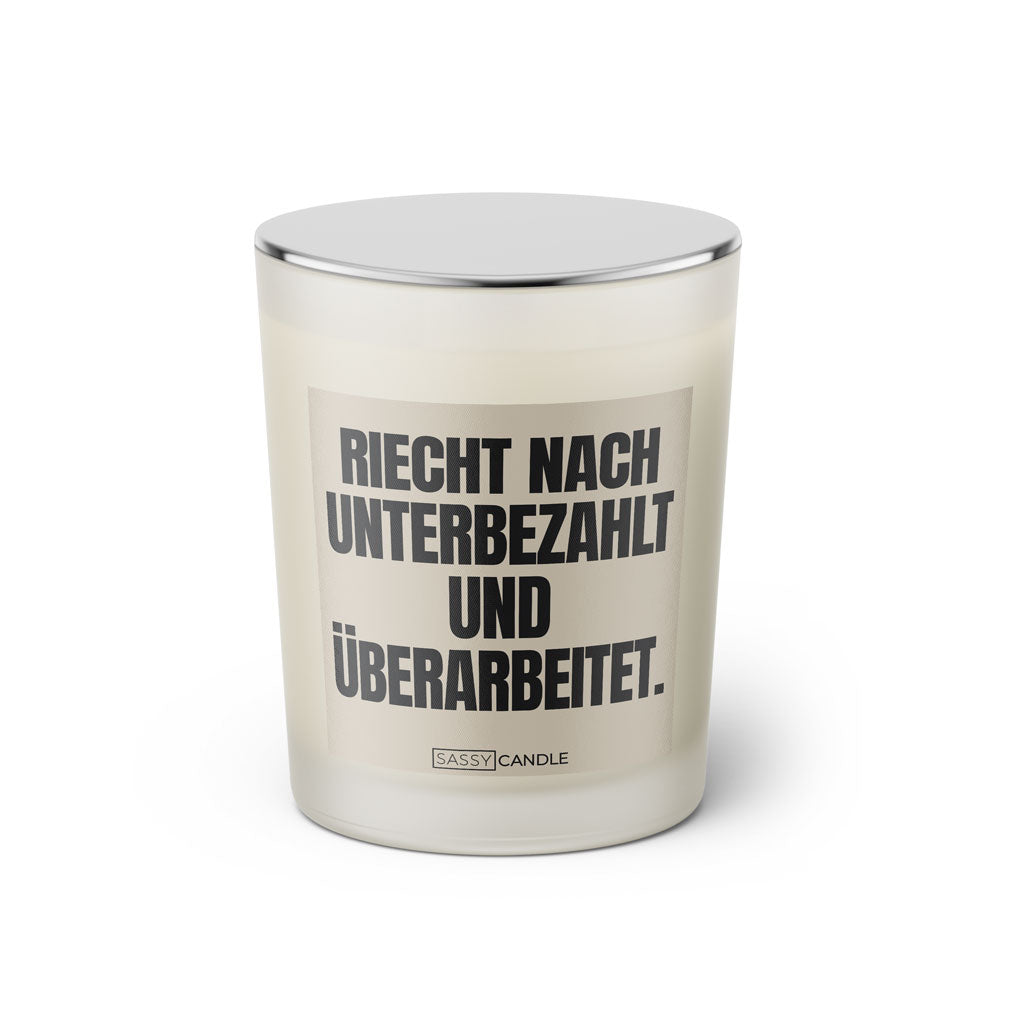 Duftkerze mit witzigem Spruch: Riecht nach unterbezahlt und überarbeitet. Farbe beige und schwarze Schrift. Kerzenglas mit silbernem geschlossenem Deckel von SassyCandle.