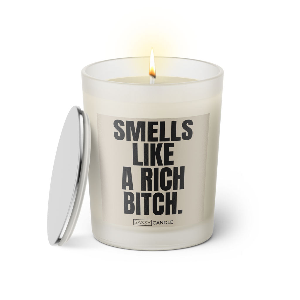 Duftkerze mit witzigem Spruch: Smells like a rich bitch. Farbe beige und schwarze Schrift. Kerzenglas mit silbernem Deckel von SassyCandle.
