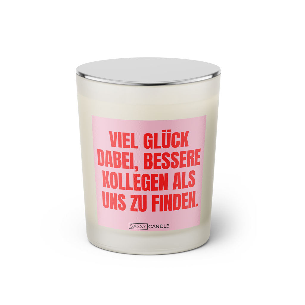 Duftkerze mit witzigem Spruch: Viel Glück dabei, bessere Kollegen als uns zu finden. Farbe rosa und pinke Schrift. Kerzenglas mit silbernem Deckel von SassyCandle.