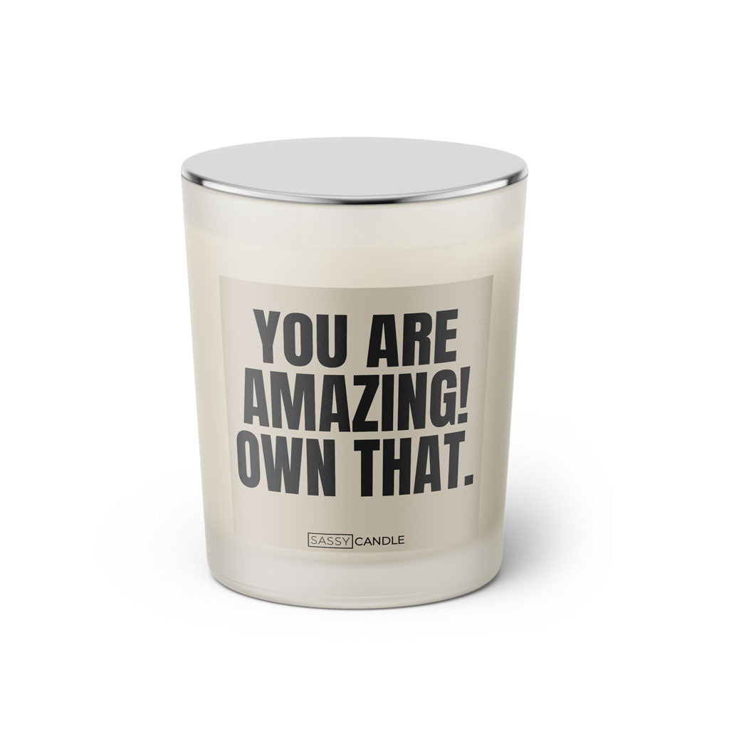 Duftkerze mit witzigem Spruch: You are amazing! Own that. Farbe beige und schwarze Schrift. Kerzenglas mit silbernem geschlossenem Deckel von SassyCandle.