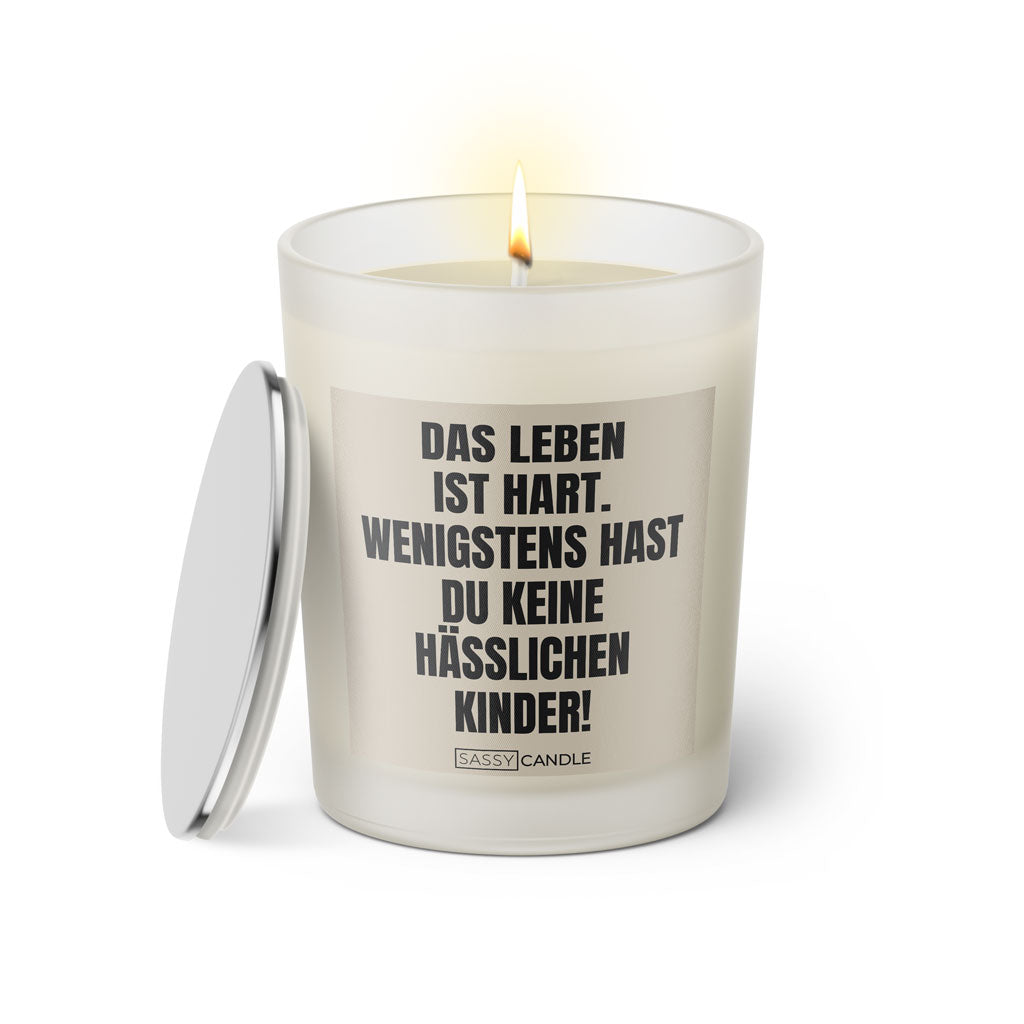 Duftkerze mit witzigem Spruch: Das Leben ist hart. Wenigstens hast du keine hässlichen Kinder. Farbe beige und schwarze Schrift. Kerzenglas mit silbernem Deckel von SassyCandle