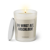Duftkerze mit witzigem Spruch: Du wirst alt Arschloch. Farbe beige und schwarze Schrift. Kerzenglas mit silbernem Deckel von SassyCandle.