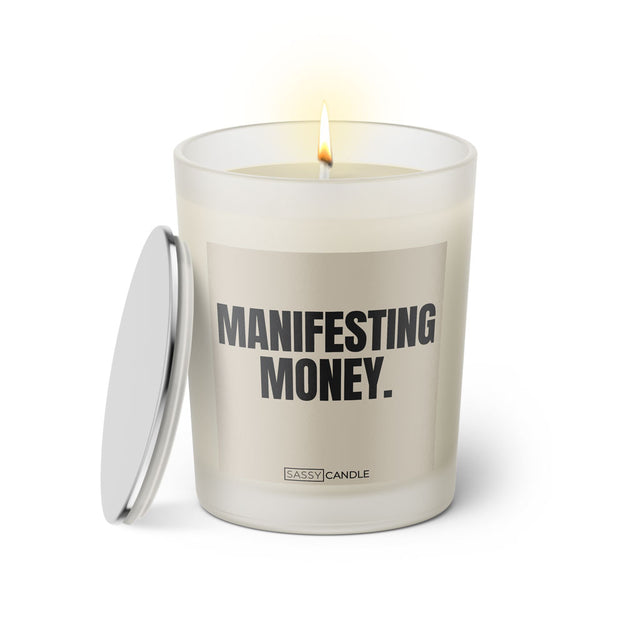 Duftkerze mit witzigem Spruch: Manifestant Money. Farbe beige und schwarze Schrift. Kerzenglas mit silbernem Deckel von SassyCandle.